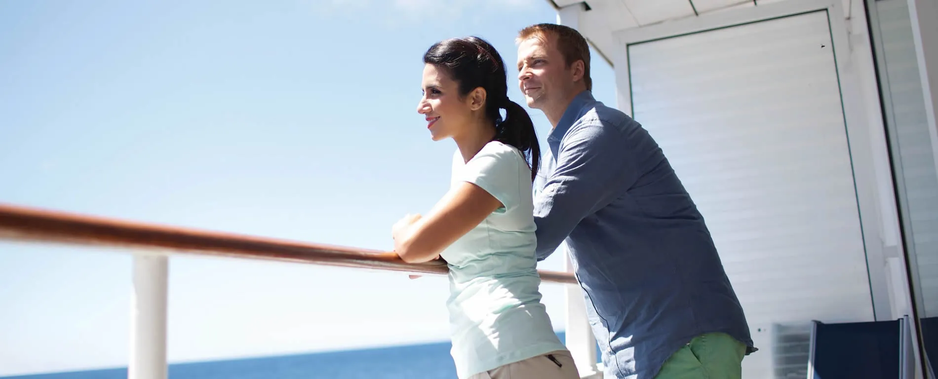 Two people enjoying view from deck, leaning on railing against blue sky