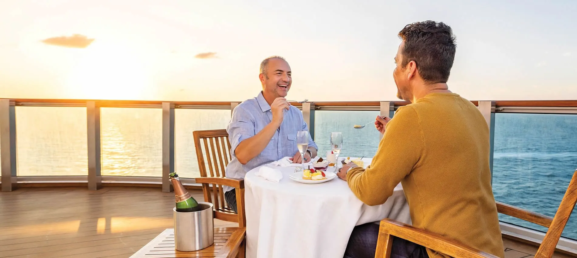 Two men enjoying dinner on a cruise ship deck at sunset