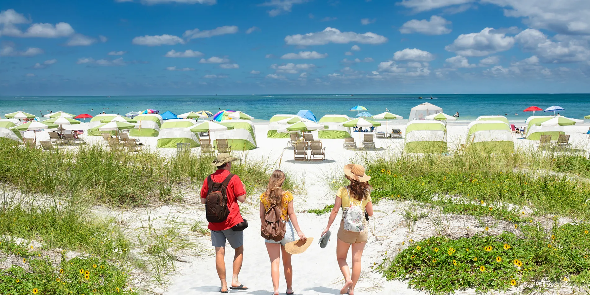 Tourists walking on sandy path towards beach with colorful umbrellas