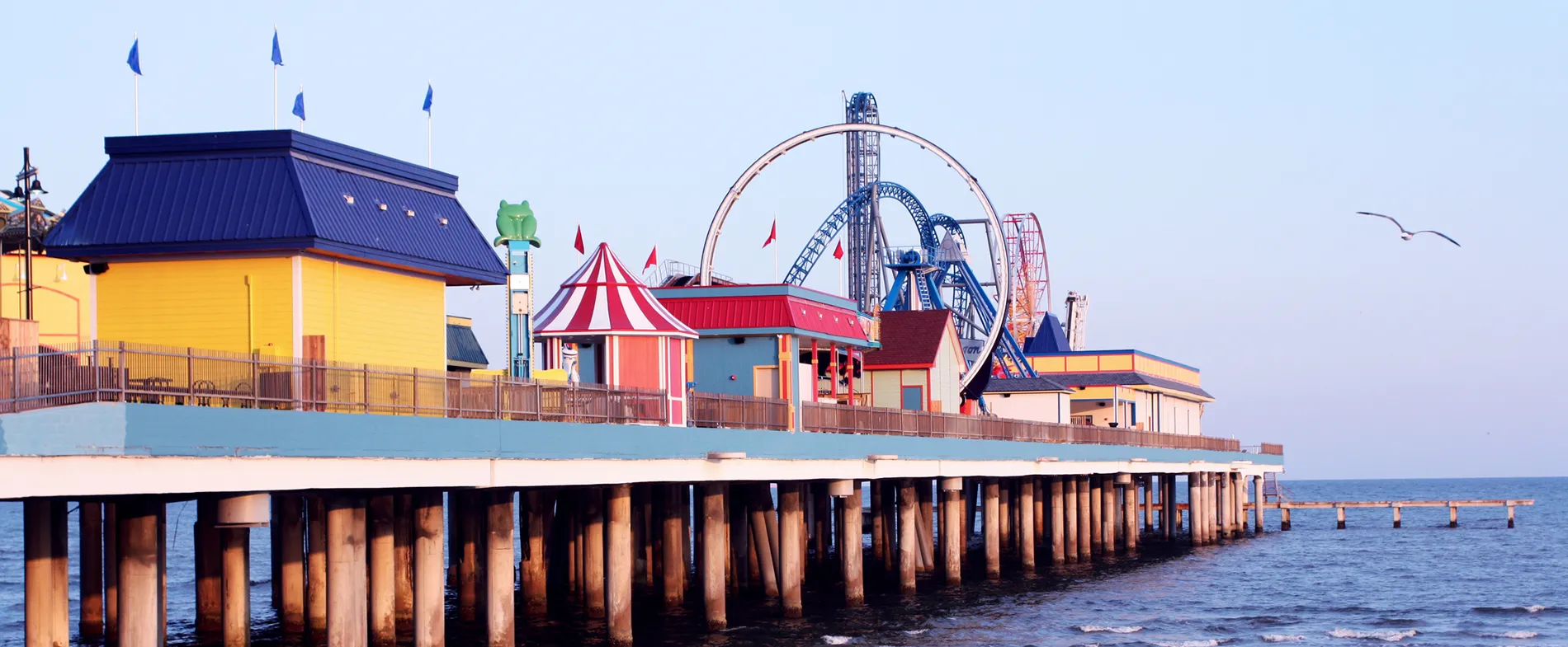 Colorful amusement park pier with roller coaster and seaside buildings