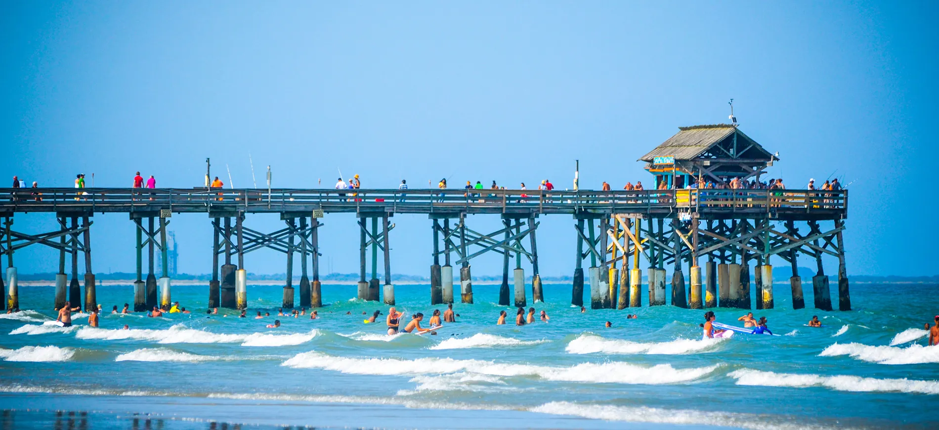Crowded wooden pier with people swimming and enjoying turquoise ocean waves