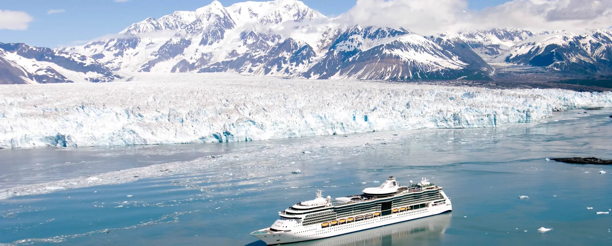 Cruise ship sailing near massive glacier and snow-capped mountains in Alaska
