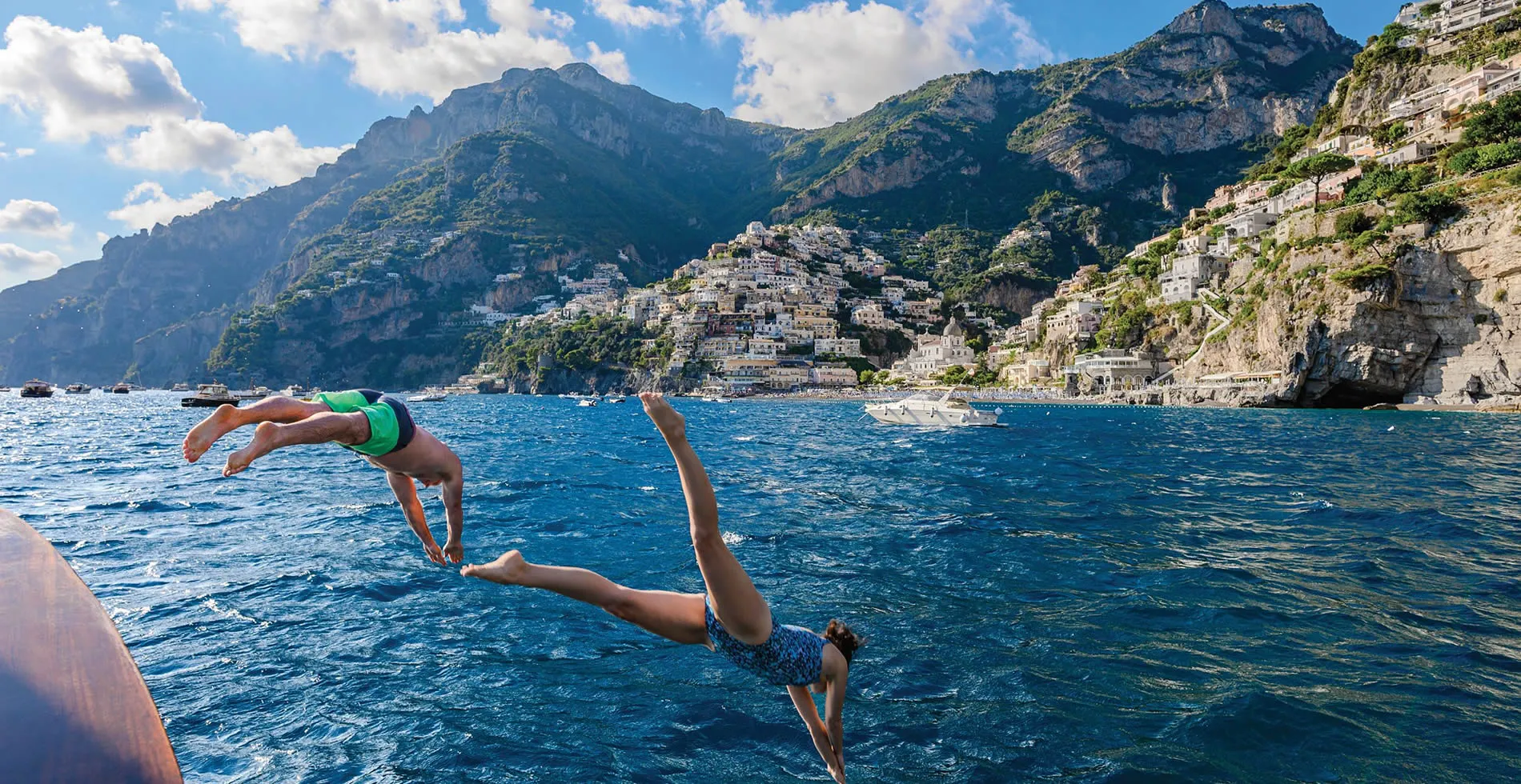 Two people diving into blue waters of Positano, with dramatic coastal mountains