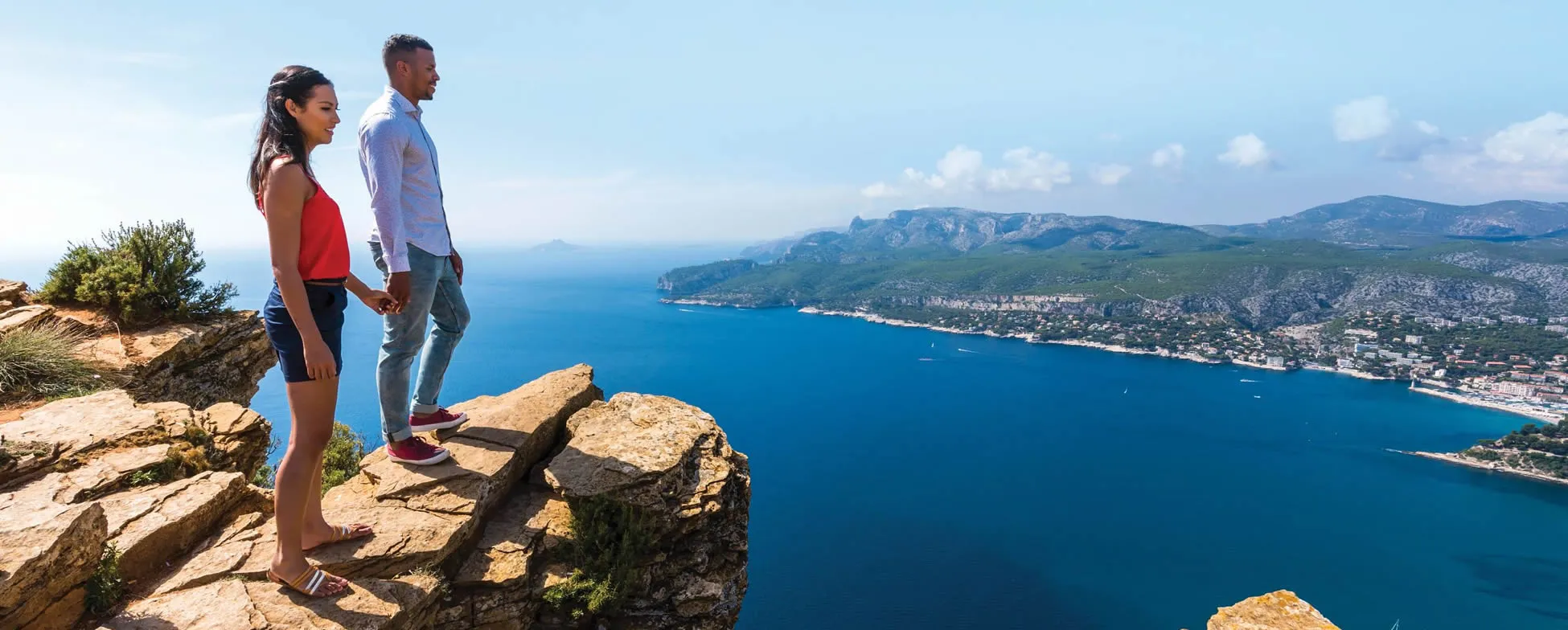 Two people overlooking stunning blue coastline and mountains from rocky cliff