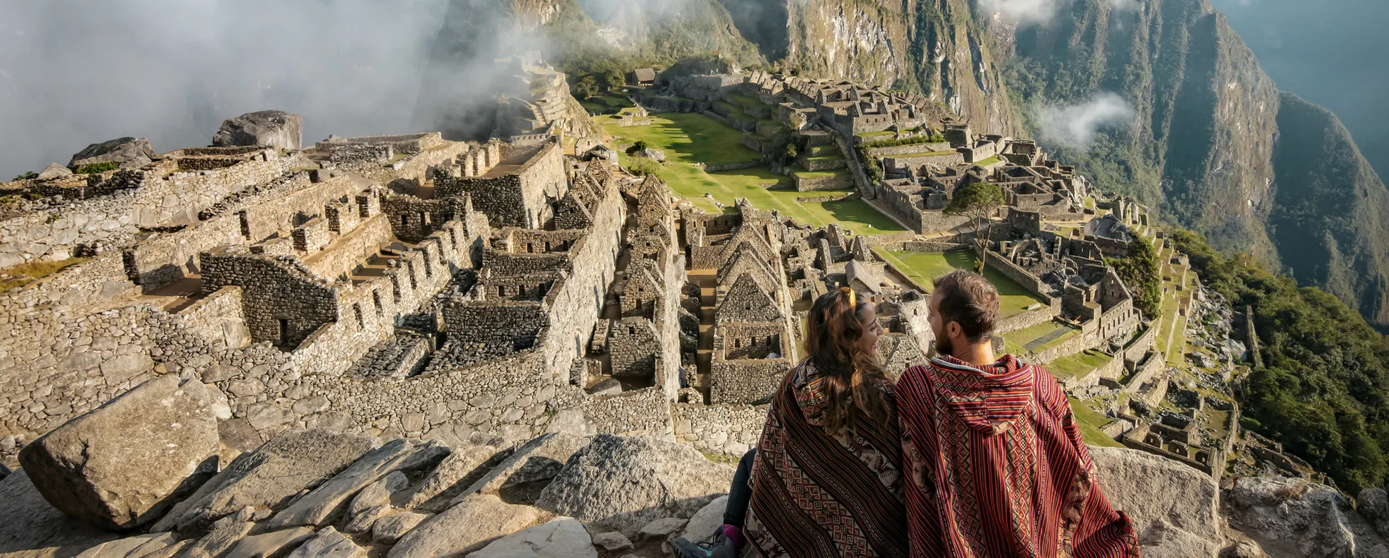 Misty Machu Picchu ruins with two travelers overlooking ancient Incan city