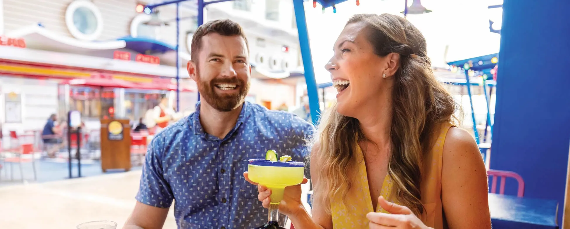Two friends laughing and enjoying yellow cocktails at a bright restaurant