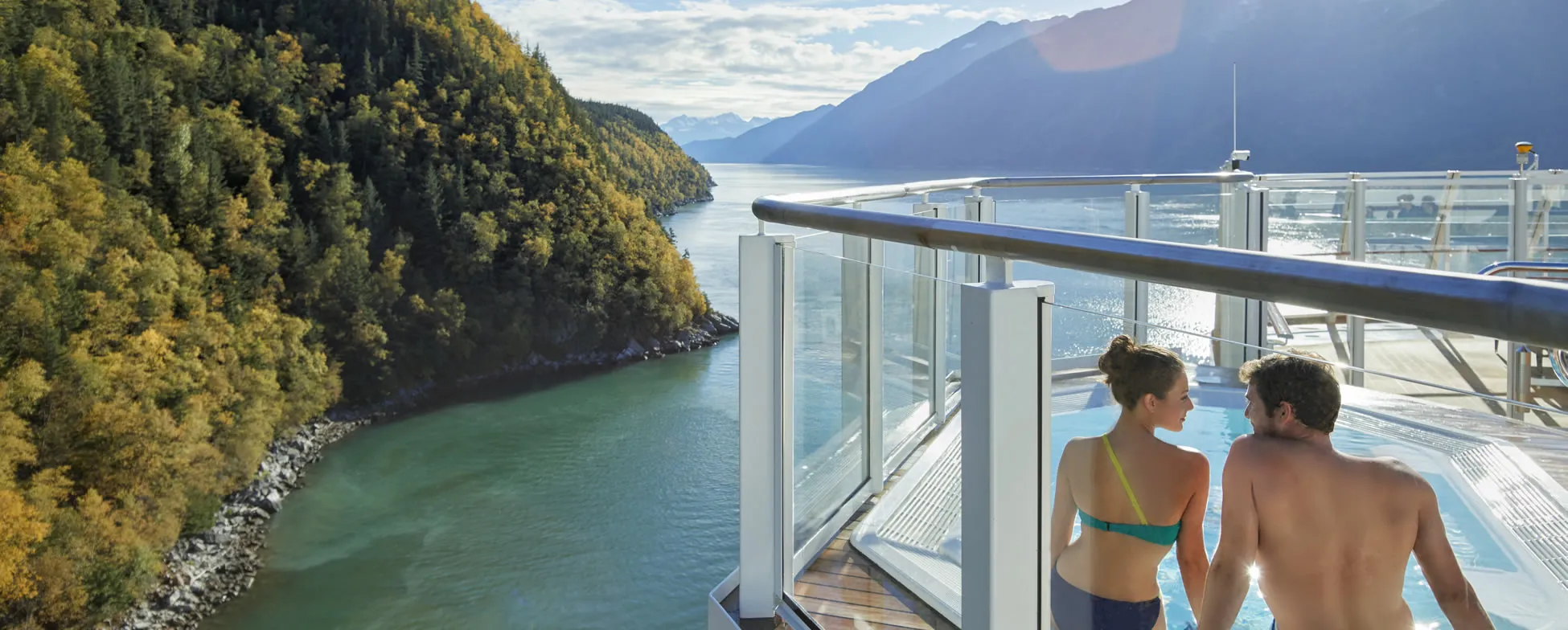 Cruise ship deck overlooking scenic fjord with forested mountains