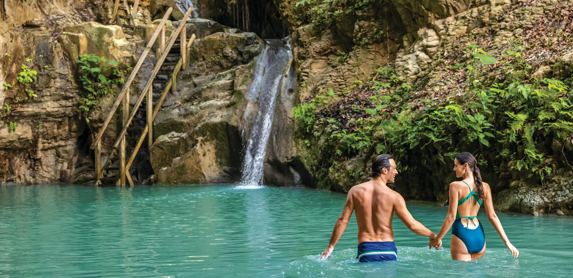 Couple swimming in turquoise waterfall lagoon with rocky backdrop