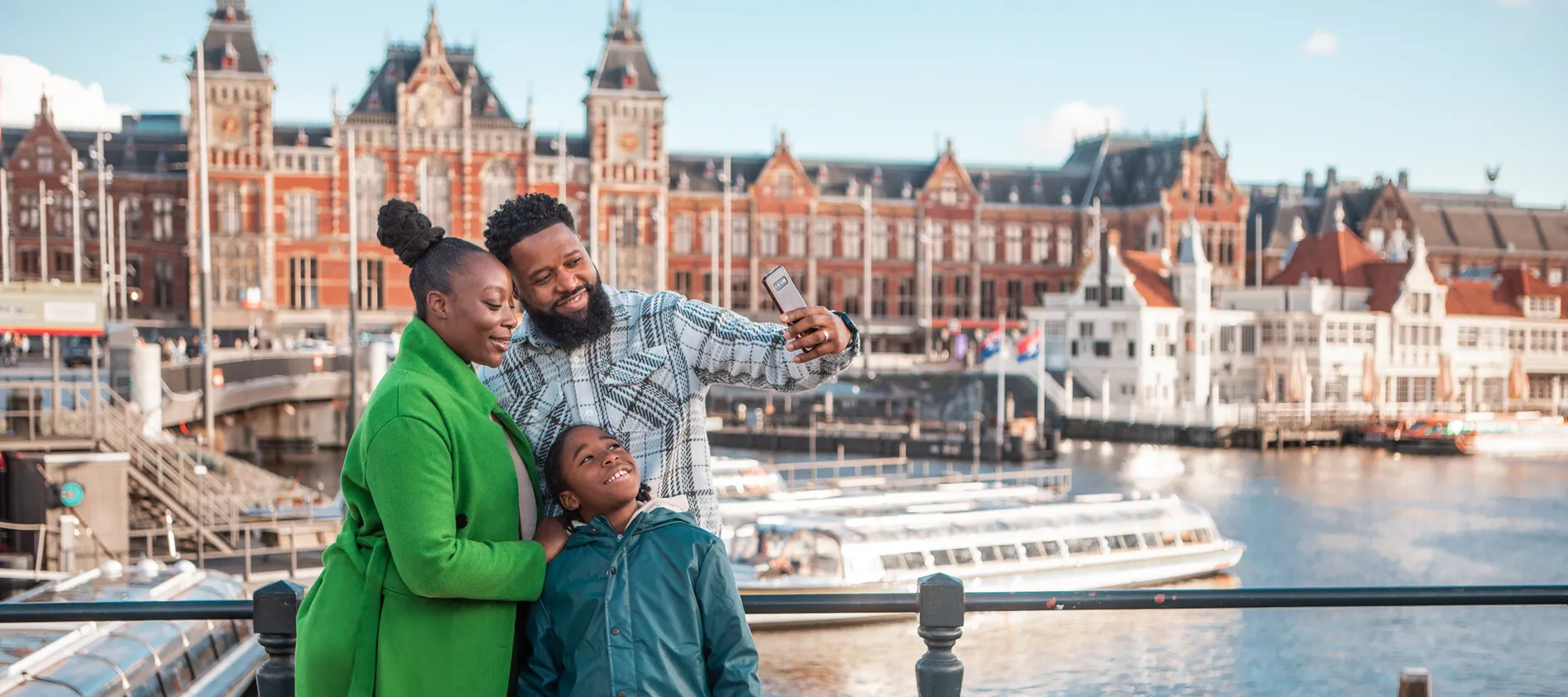 Family taking selfie at Amsterdam Central Station with canal boats