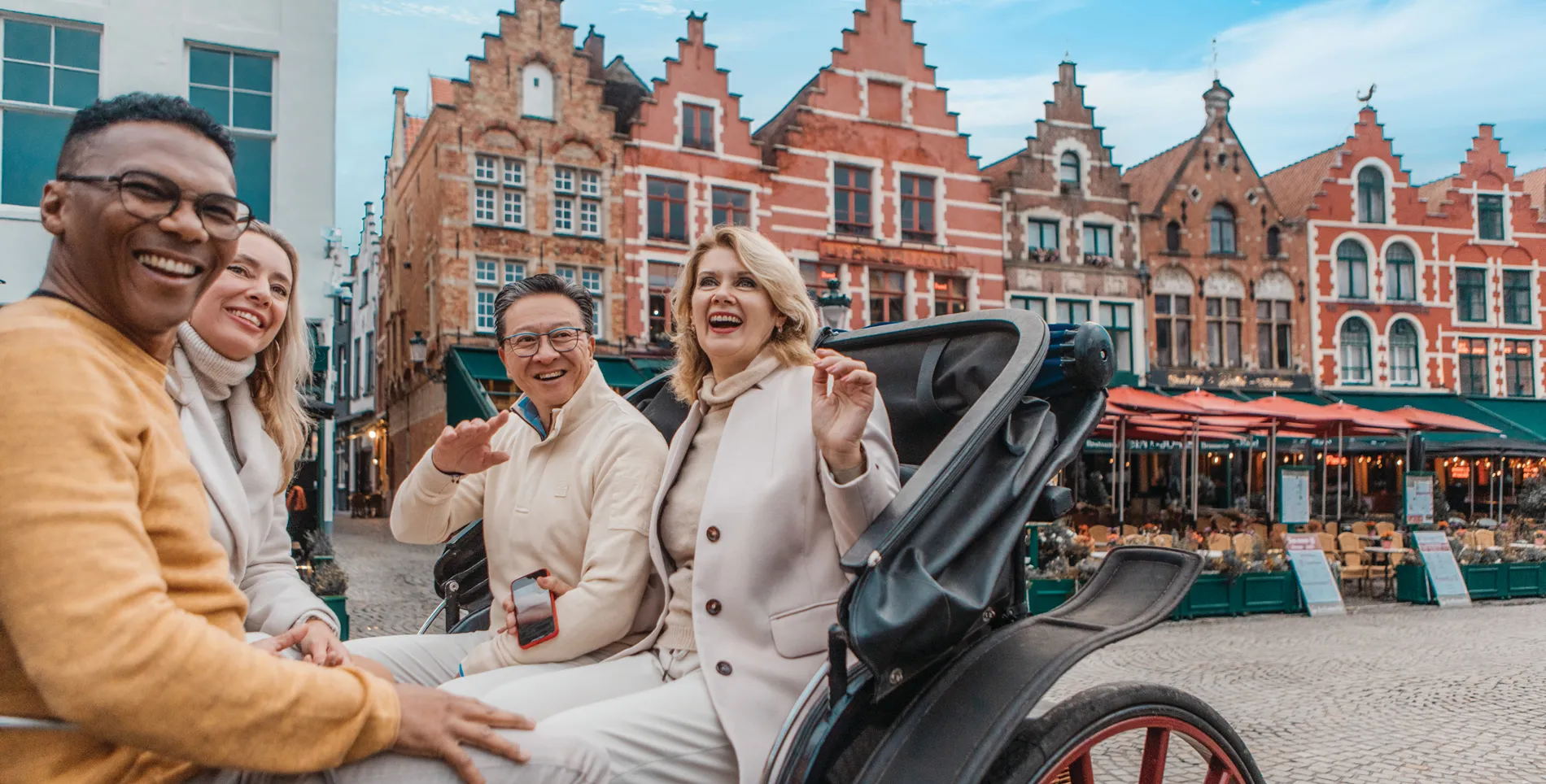 Friends enjoying carriage ride through historic Bruges with traditional Belgian architecture