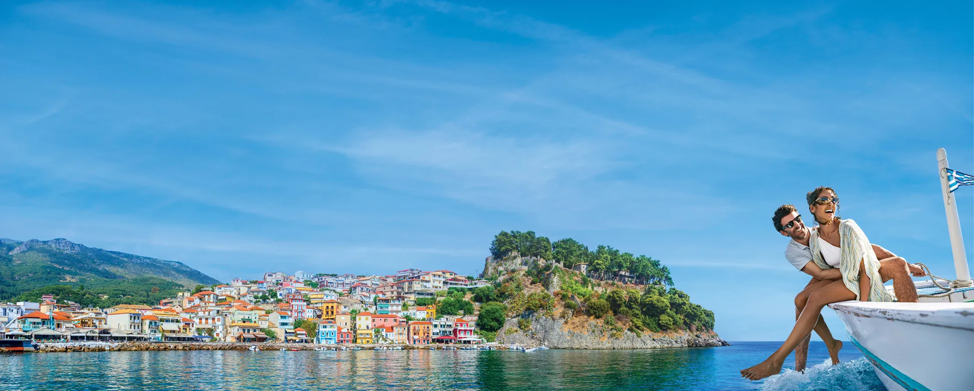 Colorful Greek coastal town with rocky island and couple on sailboat