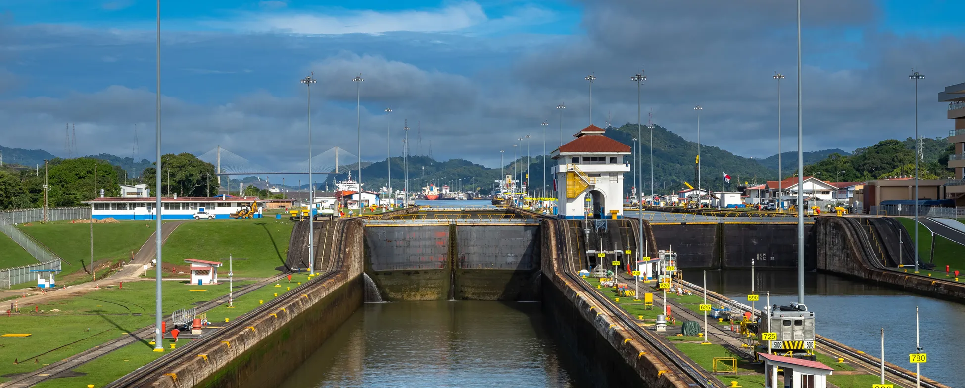 Panama Canal locks with ships, control tower, and lush mountain landscape