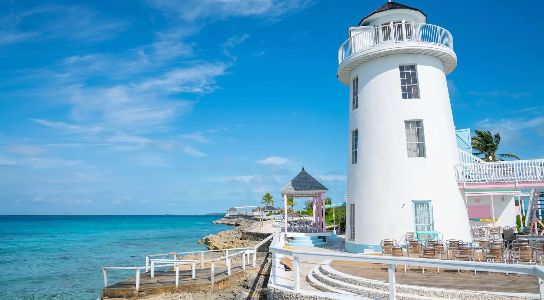 White lighthouse on rocky coastline with turquoise ocean and outdoor seating