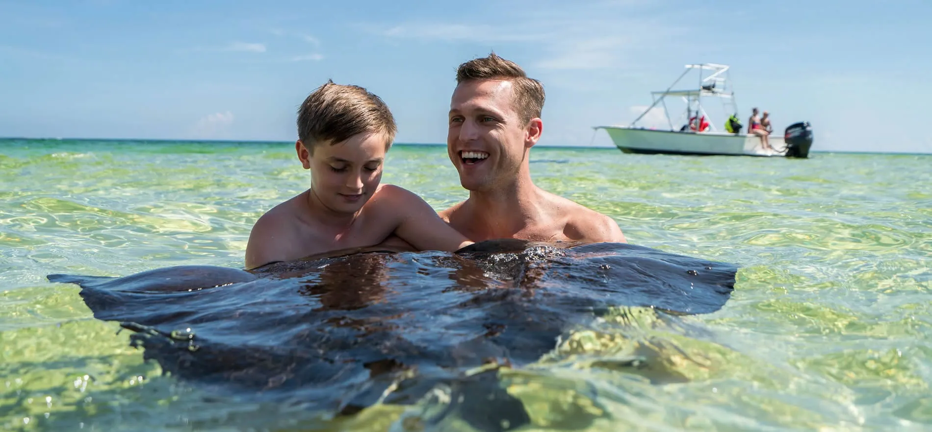 Father and son swimming with stingray in clear tropical ocean waters