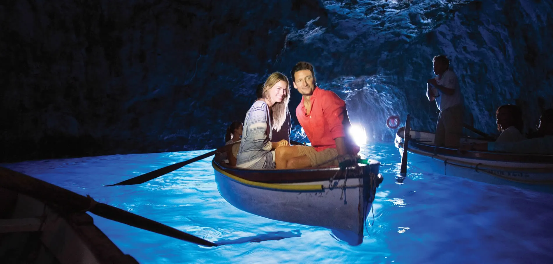 Two people in a boat inside a glowing blue cave with dramatic lighting
