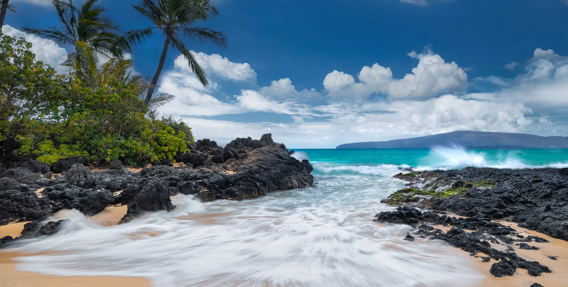 Rocky Hawaiian beach with turquoise waves, palm trees, and dramatic cloudy sky