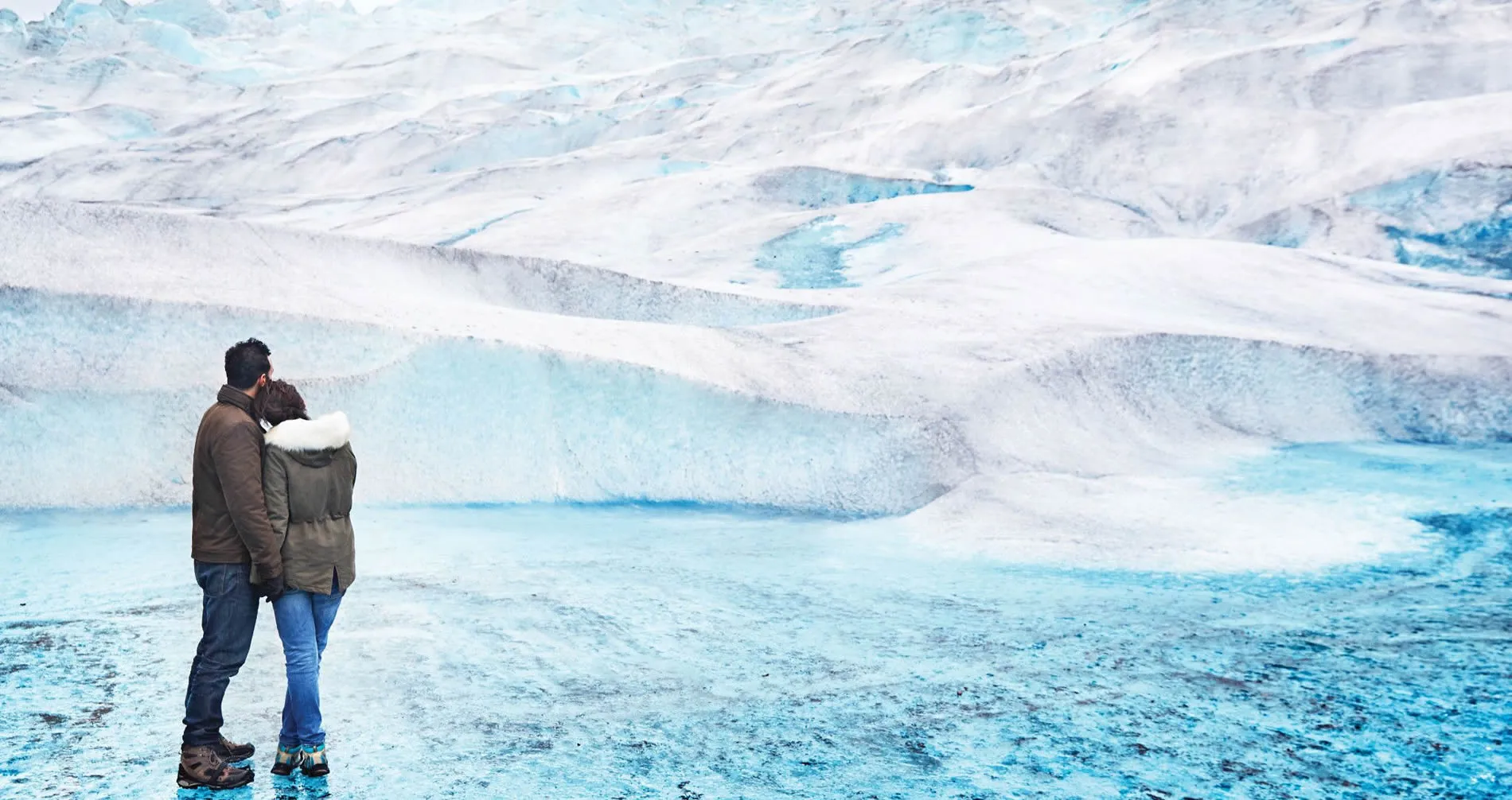 Two people standing together on a blue-white glacial landscape