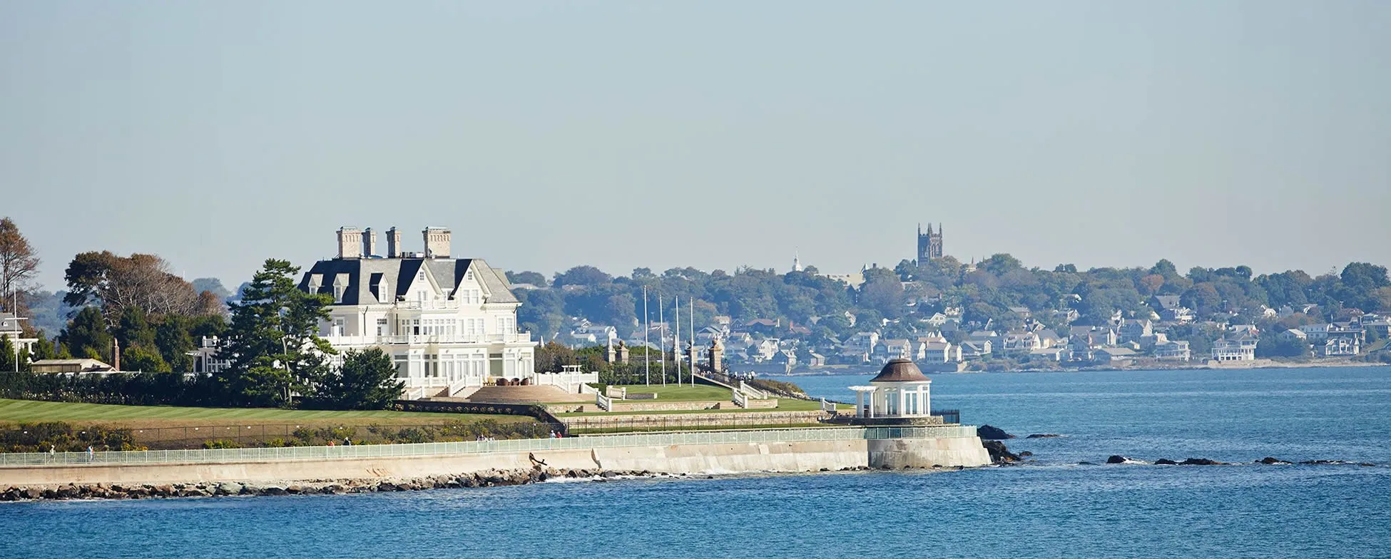 Elegant white mansion on rocky coastline with town and church in background
