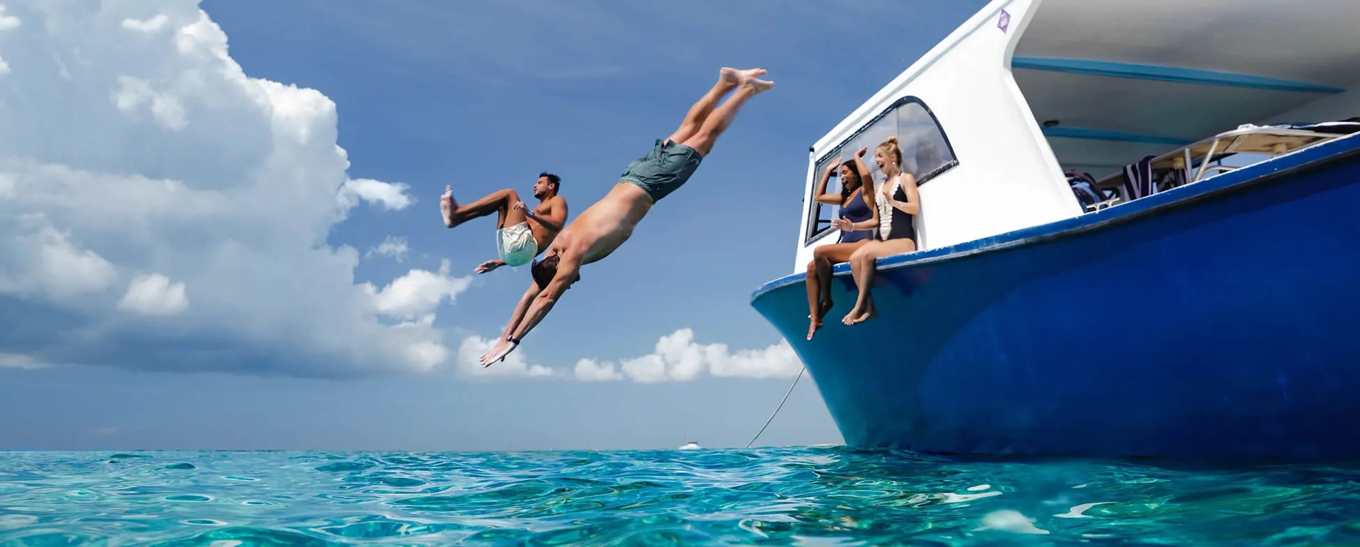 People jumping off boat into turquoise tropical waters on sunny day