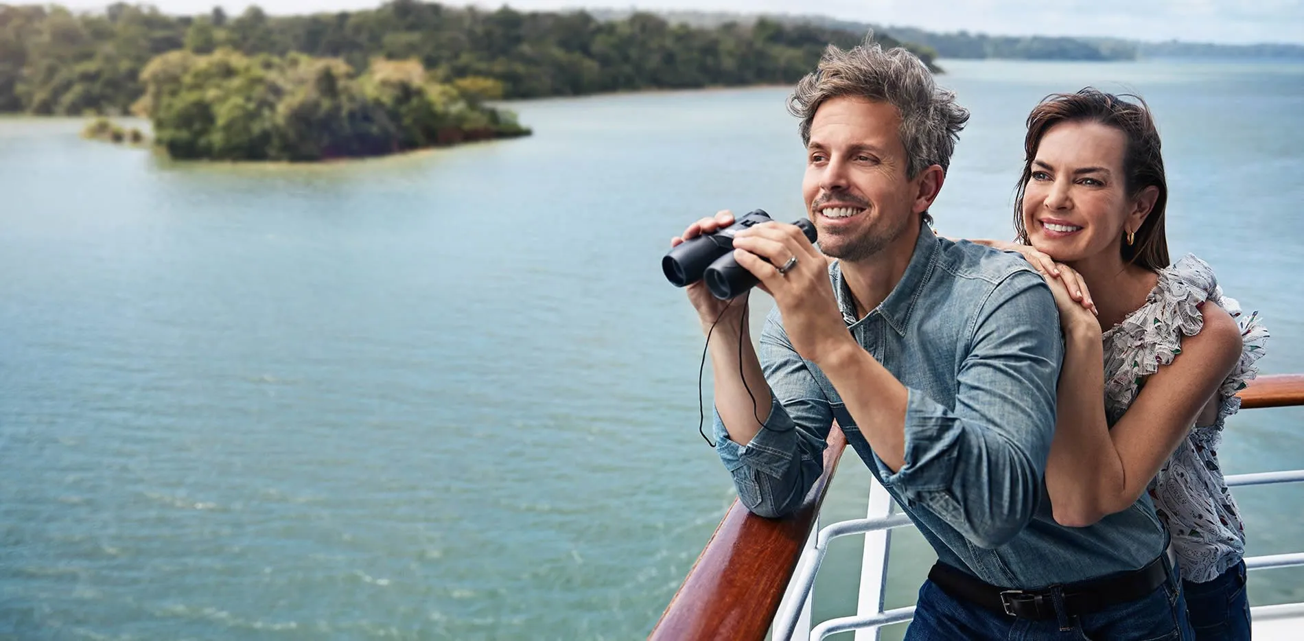 Couple using binoculars on a boat, enjoying scenic lake and forest view