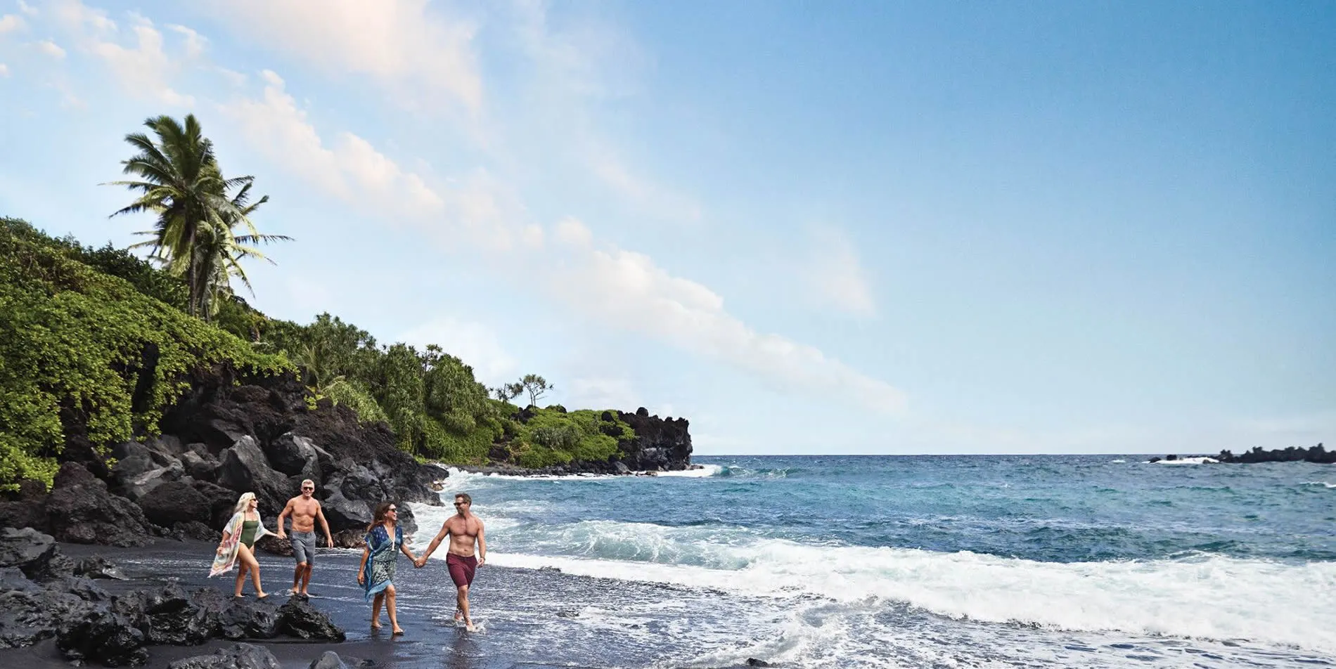 Group walking on rocky black sand beach with palm trees and ocean