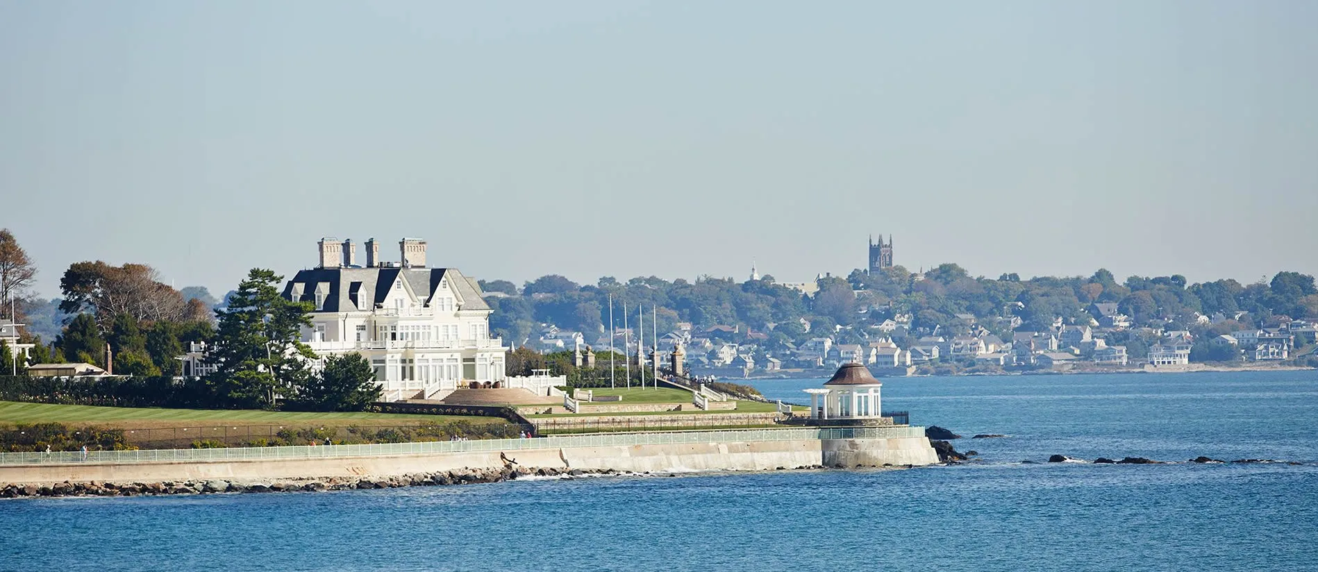 Elegant white mansion on rocky coastline with seaside town in background