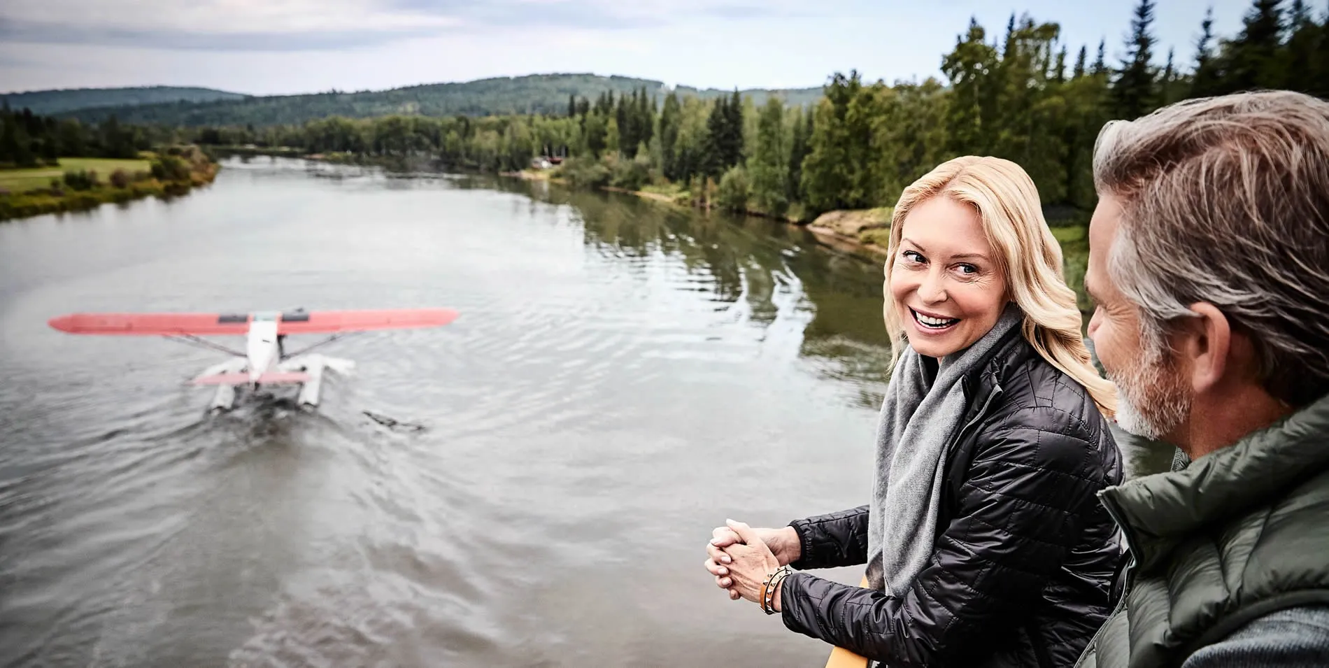 Smiling woman and companion watching seaplane on forest river