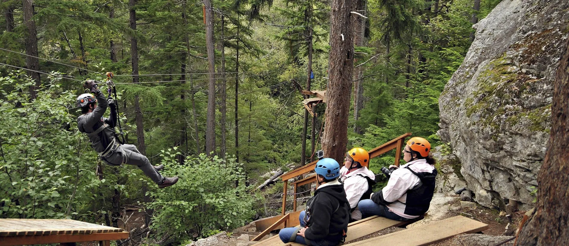 Ziplining through lush forest with safety-geared participants watching
