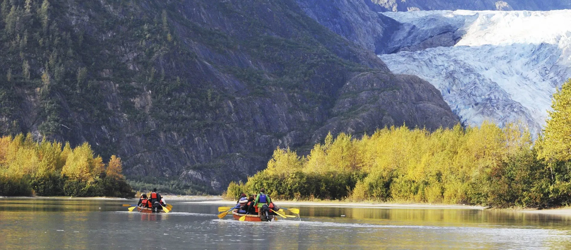 Rafters paddling on river with glacier and autumn trees in background