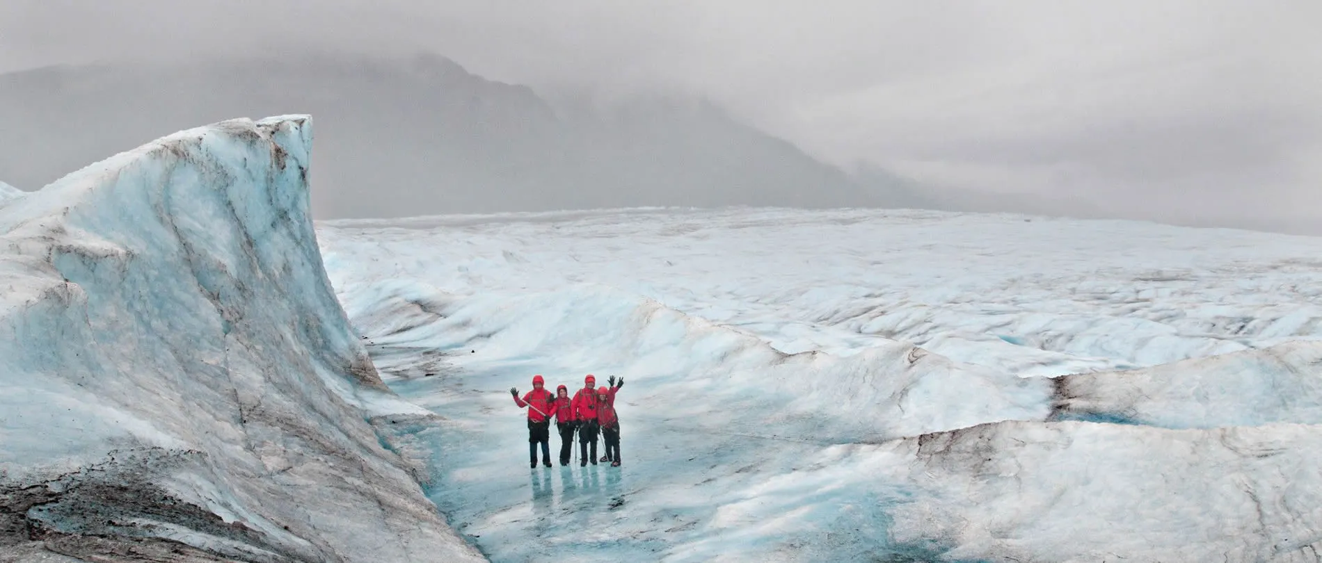 Hikers in red jackets standing on a vast, blue-white glacial landscape