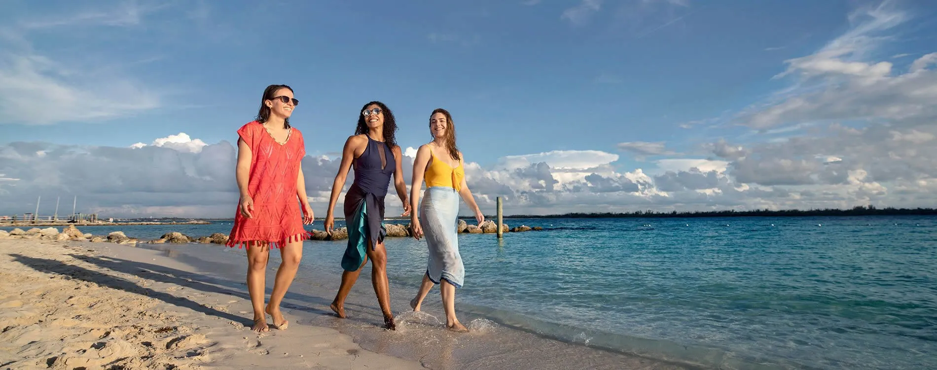 Three friends walking together on a sunny beach with blue ocean