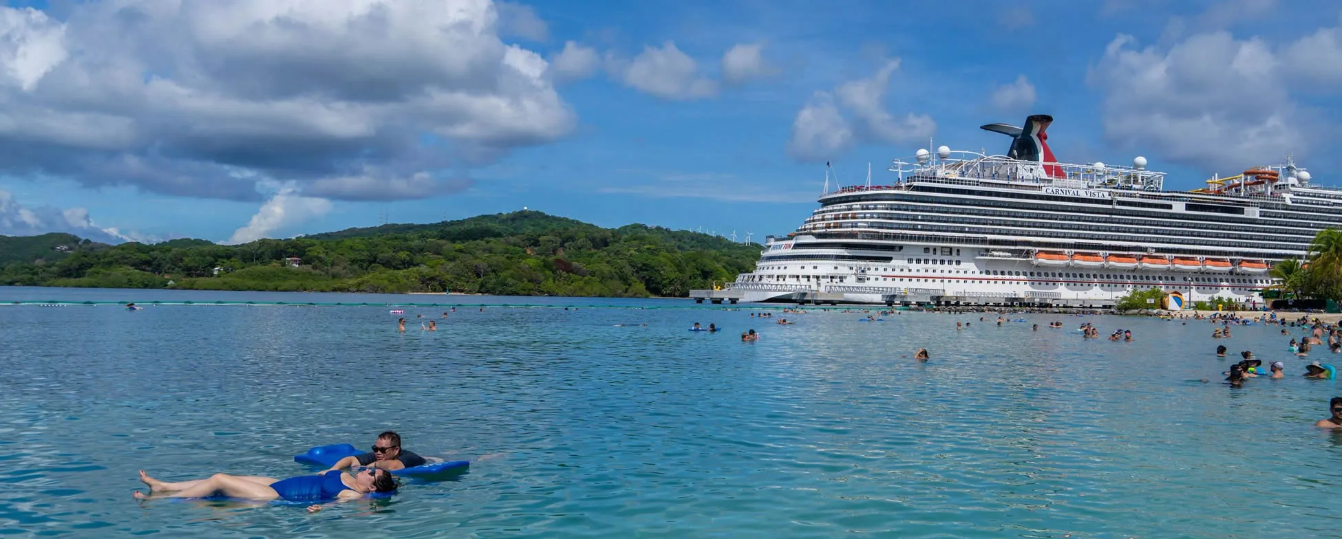 Cruise ship docked at tropical beach with people swimming in turquoise water