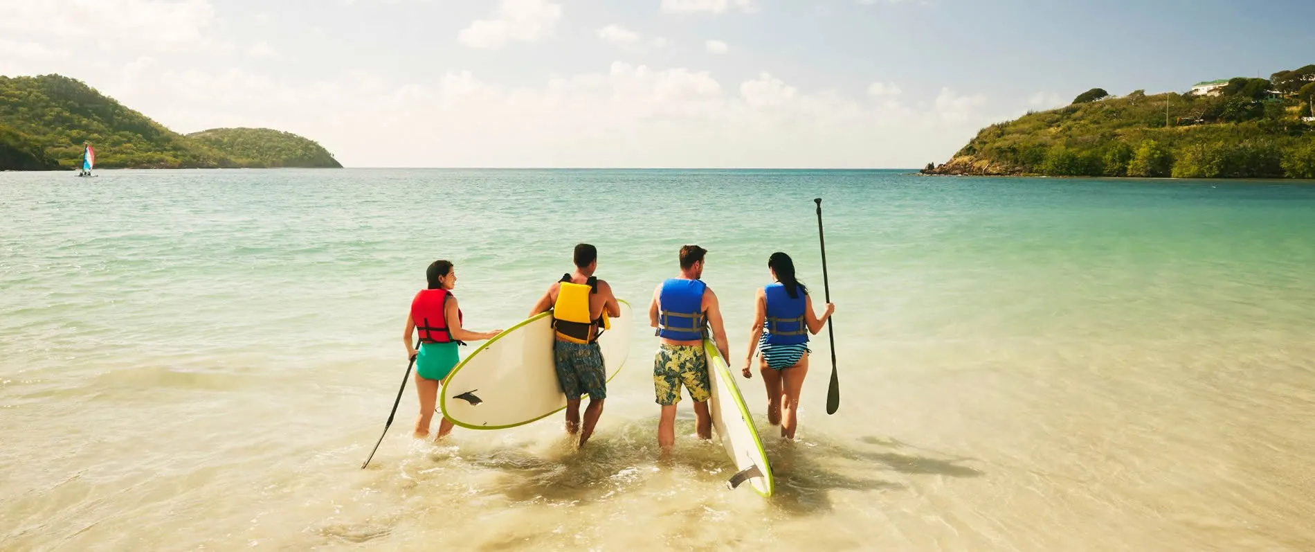 Four paddleboarders walking into turquoise water with lush islands behind