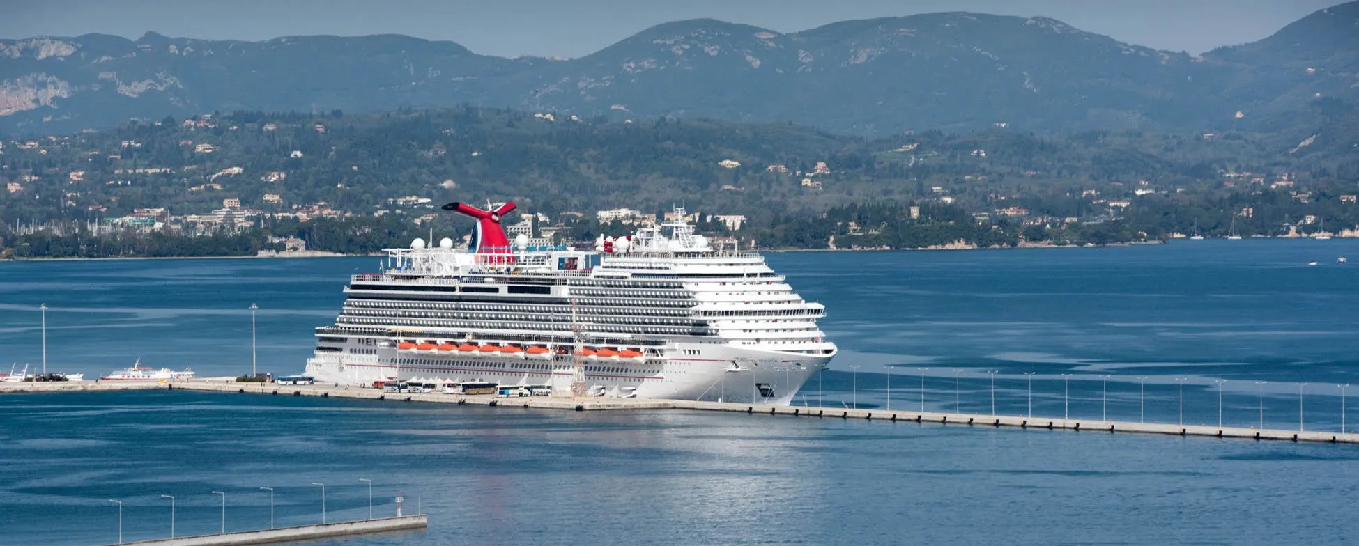 Large cruise ship docked in scenic mountain bay with blue water