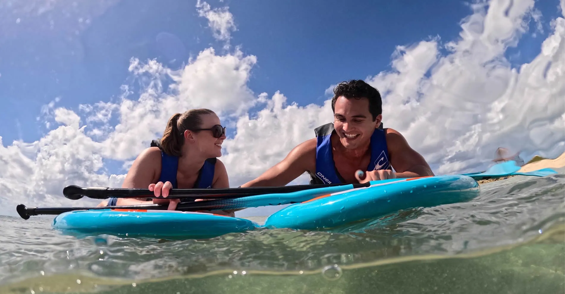 Two people paddleboarding together on bright blue boards under cloudy sky