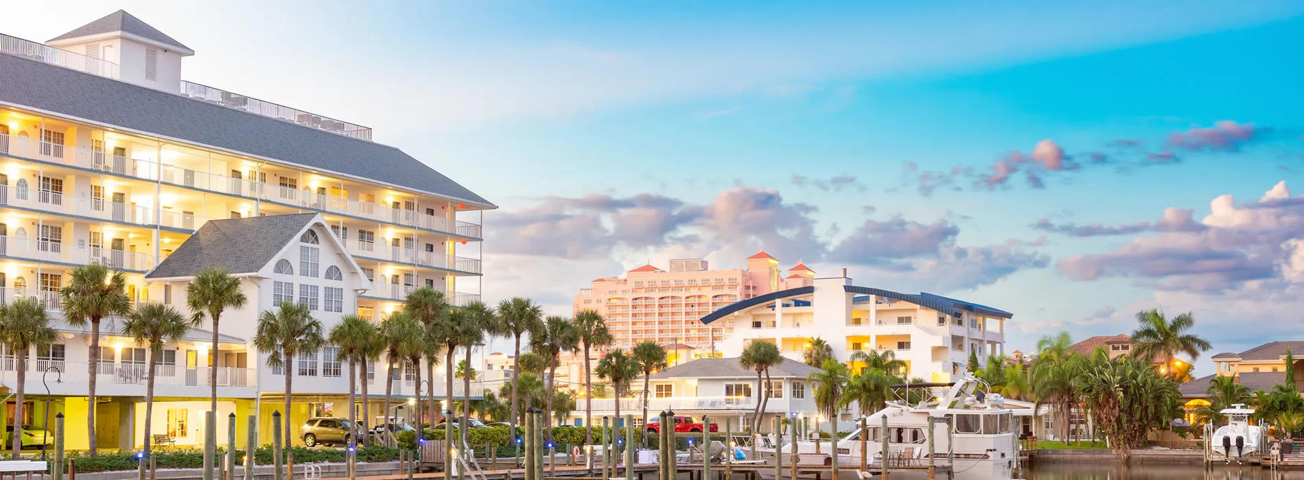 Coastal resort with palm trees, boats, and multi-story buildings at sunset