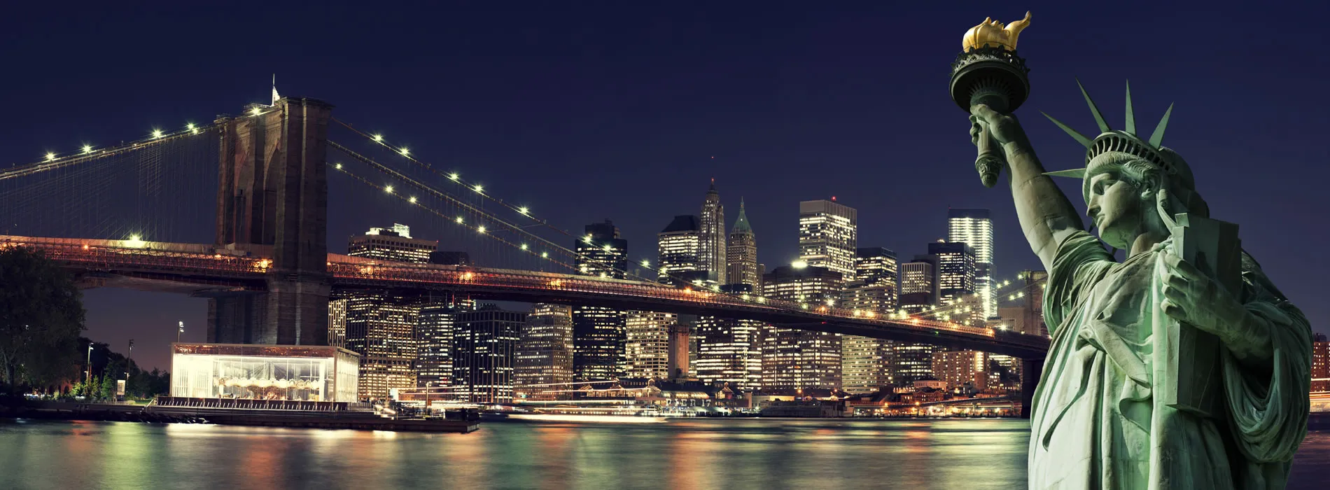 New York City skyline at night with Brooklyn Bridge and Statue of Liberty