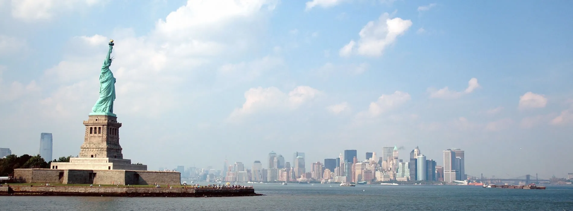 Statue of Liberty with New York City skyline in background on sunny day