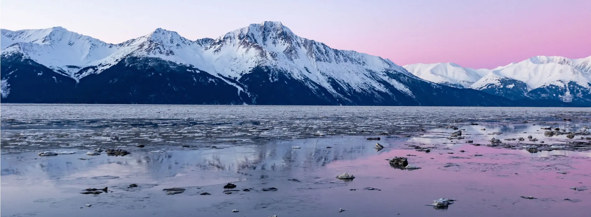 Snow-capped mountains reflecting in icy water at pink twilight