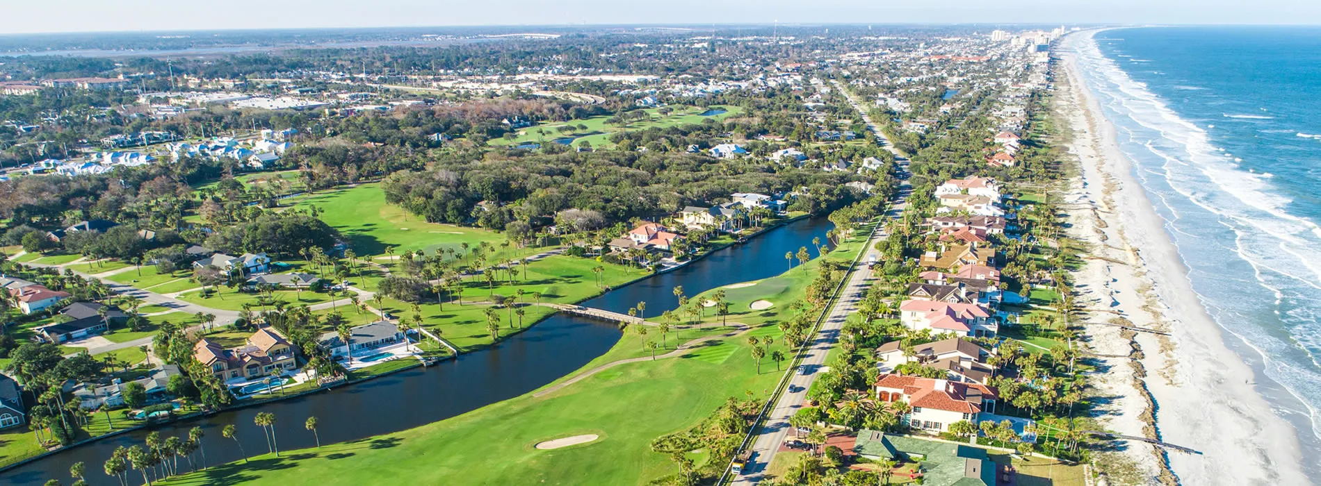 Aerial view of coastal golf course community with waterway and ocean