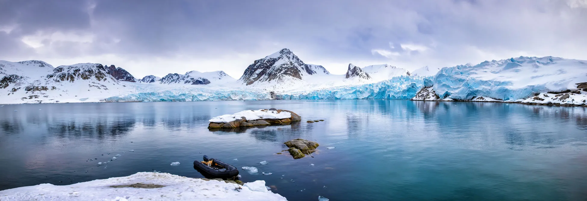 Icy arctic landscape with blue glacier, rocky islands, and inflatable boat
