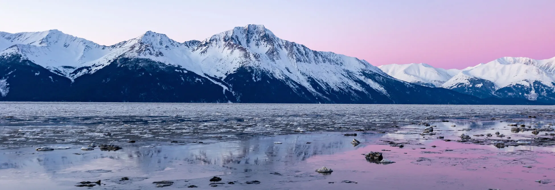 Snowy mountains reflecting in icy water at pink twilight