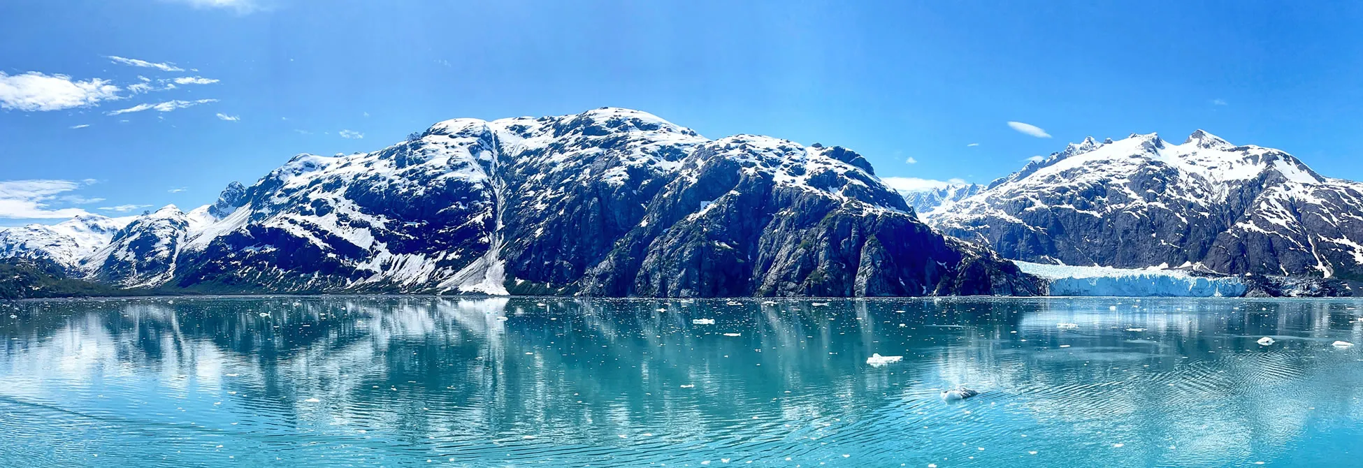 Snow-capped mountains reflecting in calm turquoise waters of Glacier Bay