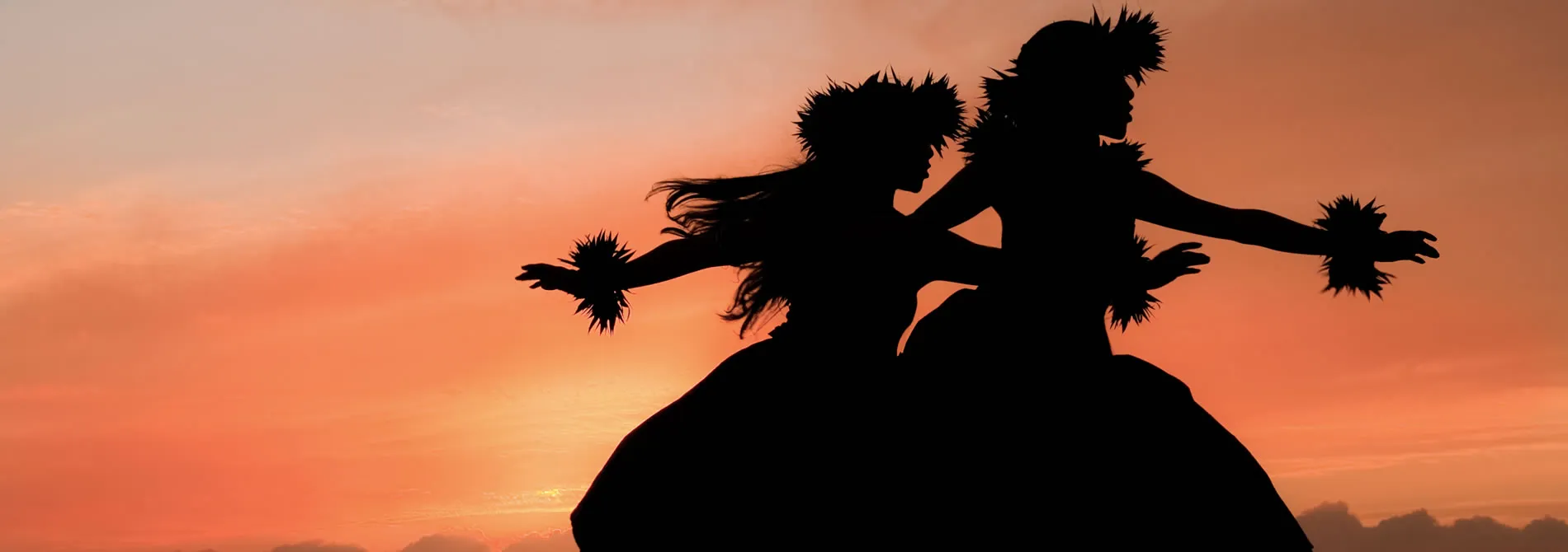 Silhouetted cheerleaders with pom-poms dancing against sunset sky