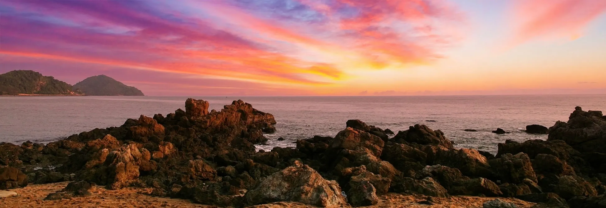Dramatic sunset over rocky coastline with vibrant pink and orange sky