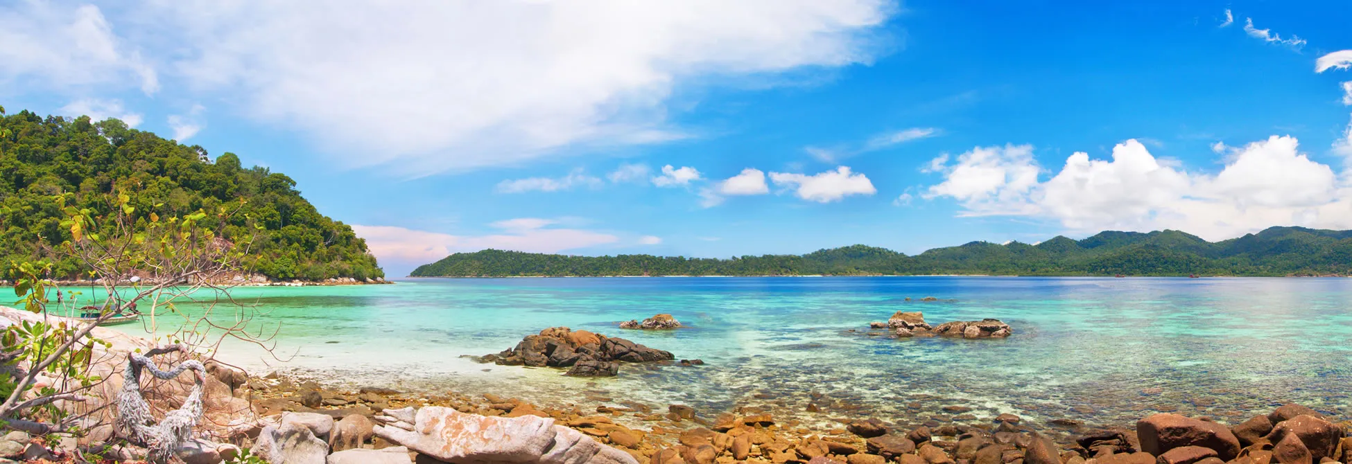 Tropical paradise with turquoise waters, rocky shore, and lush green mountains