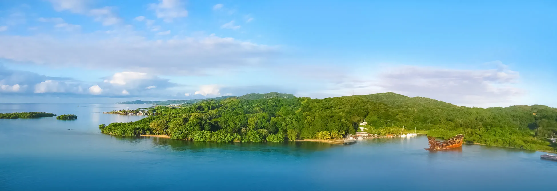 Lush green tropical island with shipwreck, blue waters, and distant mountains