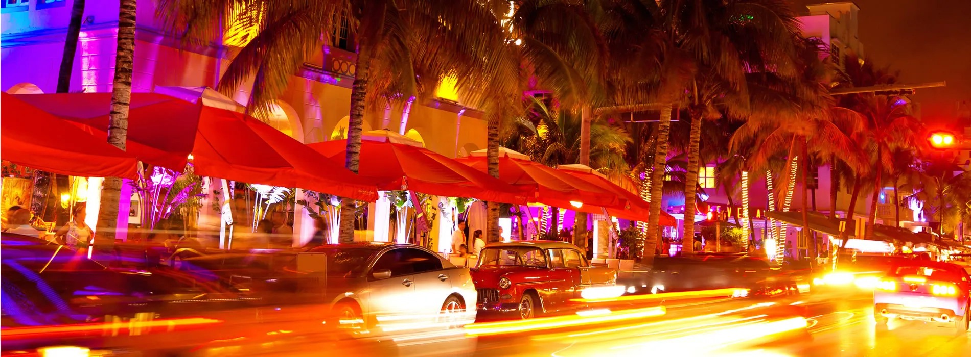 Vibrant Miami nightlife with palm trees, red umbrellas, and blurred cars