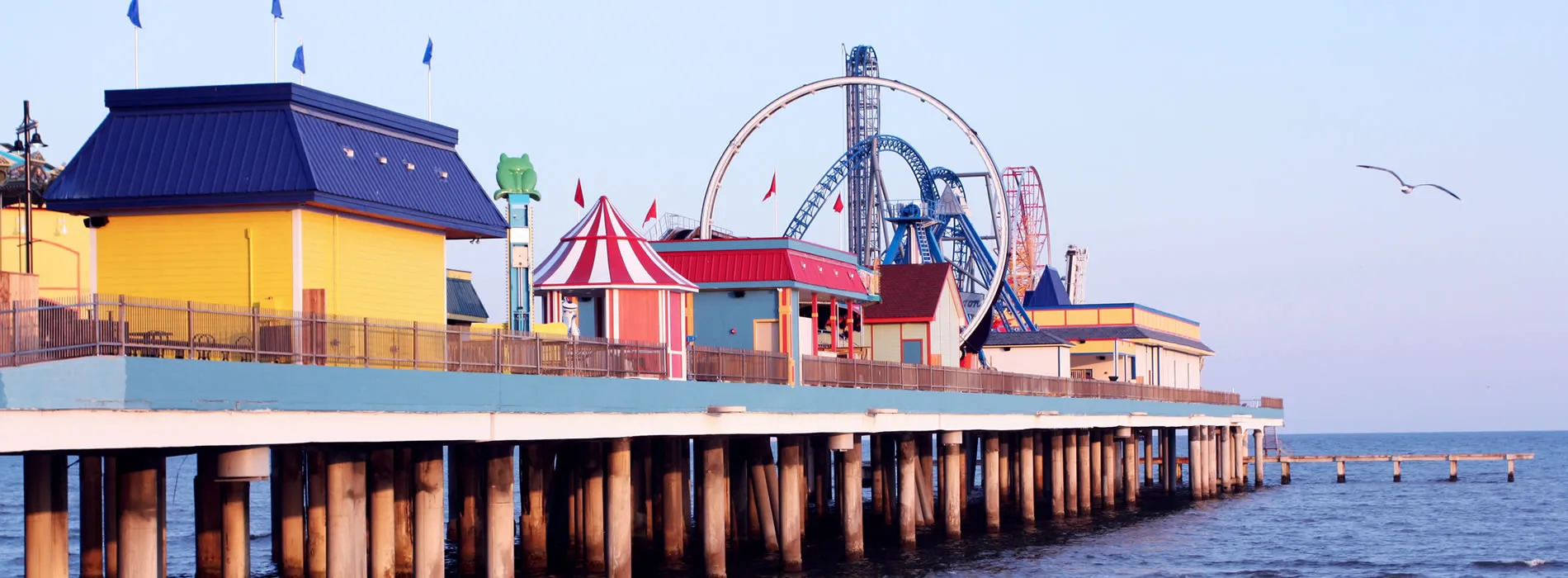 Seaside amusement park with colorful buildings and roller coaster on wooden pier