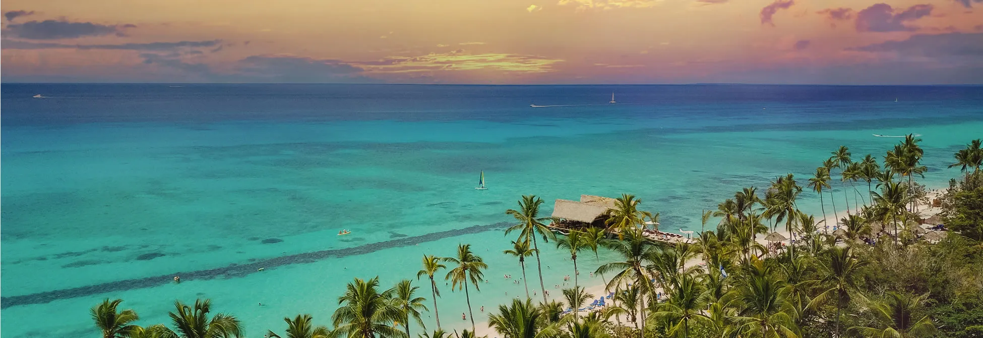 Tropical paradise with turquoise waters, palm trees, and sailboats at sunset